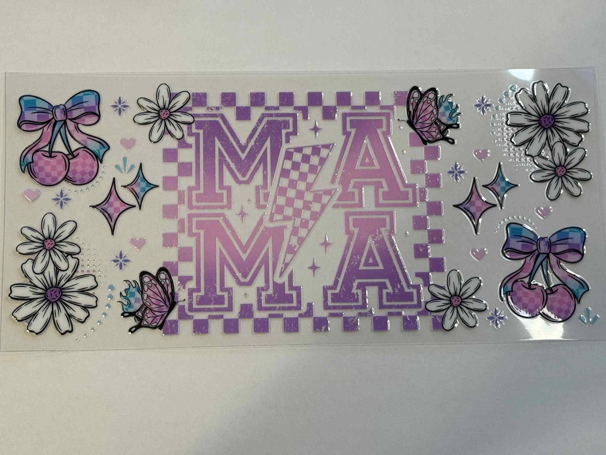 Decorative sticker sheet with letters 'MA', flowers, and bows on a checkered background.